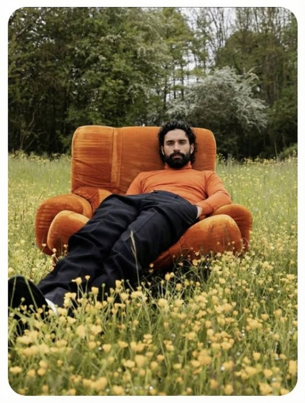 Amos Le Blanc reclining in an orange armchair set in a field of yellow flowers